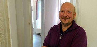 Achim steht freudig in seiner neuen Altbauwohnung.