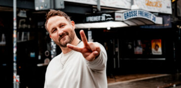 Florian Künstler zeigt ein "Peace"-Zeichen in die Kamera und lächelt.