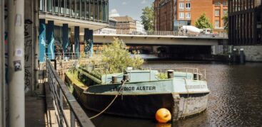 Im Innern der grünen Schute, die auf Höhe Admiralitätsstraße 10 ankert, wachsen sogar Wasserpflanzen, da die Unterseite geöffnet ist. Foto: Miguel Ferraz
