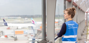 Eine blonde Frau schaut auf das Flugfeld, auf ihrer blauen Warnweste steht "Diakonie Hamburg. Abschiebungsbeobachtung"
