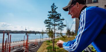 Ein Mann mit schwarzer Mütze und blauer Adidas-Jacke schaut von einem Balkon auf die Elbe