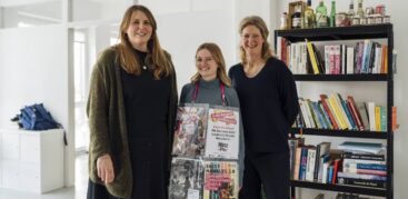 Drei lachende Frauen, eine hat Hinz&Kunzt-Plakate in einem Plastikdisplay um den Hals hängen