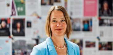 Eine Frau im hellblauen Blazer steht vor einer Wand mit Seiten aus dem Hinz&Kunzt-Magazin