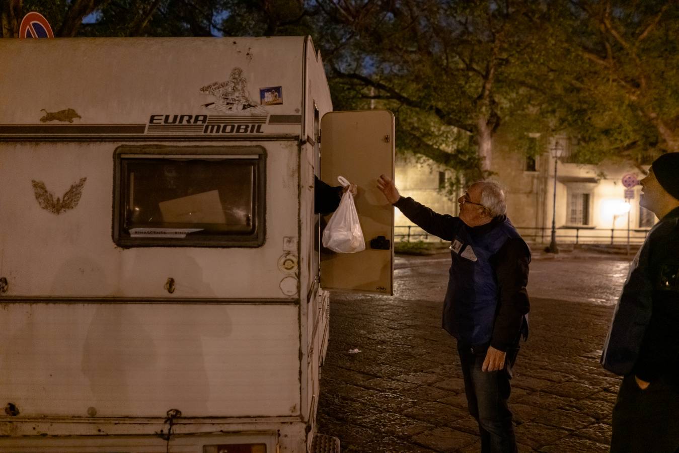 Ein Mann nimmt eine Plastiktüte entgegen, die ihm jemand aus einem Wohnwagen reicht