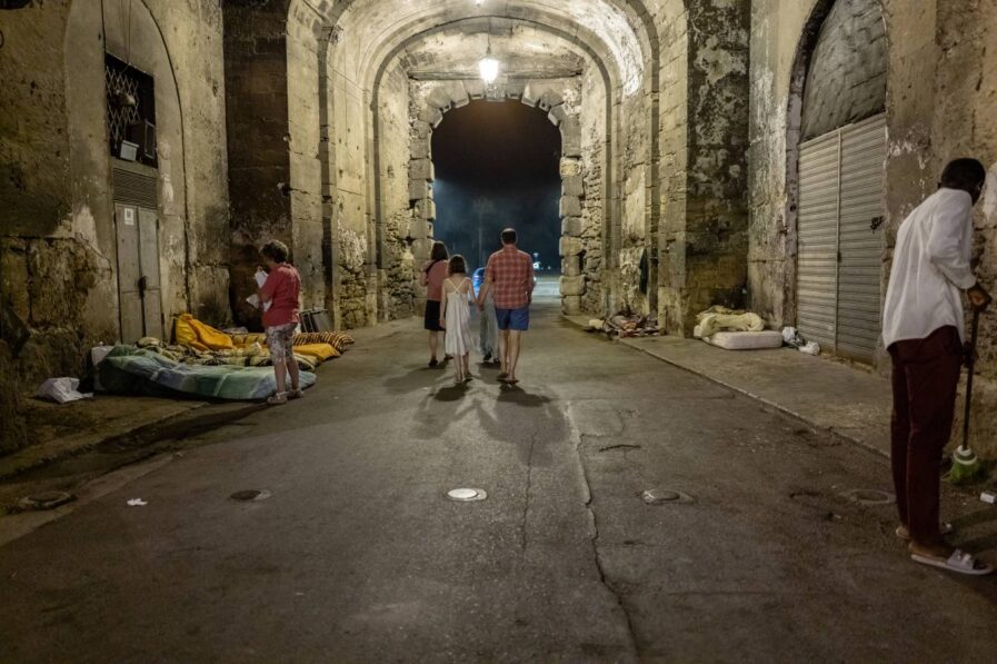Touristen spazieren unter der „Porta dei Greci“ hindurch. Der angrenzende Platz ist das Zuhause von etwa 30 obdachlosen Migranten. Foto: Giovanni Lo Curto