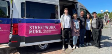 5 Menschen stehen vor einem Kleinbus und schauen in die Kamera.