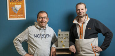 Zwei Männer schauen in die Kamera, neben ihnen ein Plakat vom Norden Festival