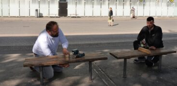 Zwei Männer mit Akkuschraubern knien neben Sitzbänken