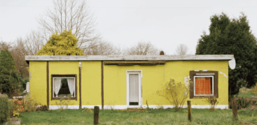 Ein heruntergekommener gelb-grüner Flachbau neben Nadelbäumen