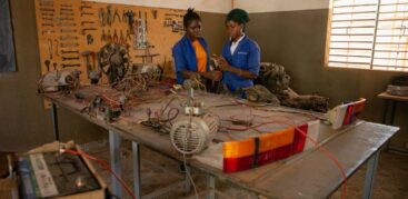 Zwei Frauen in einer Werkstatt, auf dem Tisch Motoren und Autobatterien