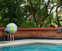 Neben einem Pool sitzt eine Frau, die einen riesigen Globus aufpustet