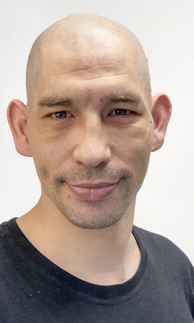 Ein Mann mit Glatze im schwarzen T-Shirt schaut lieb in die Kamera