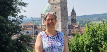 Eine Frau im bunten Kleid steht vor einem gemauerten Turm.