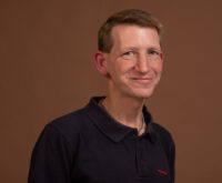 Ein blonder Mann im Polohemd lacht in die Kamera