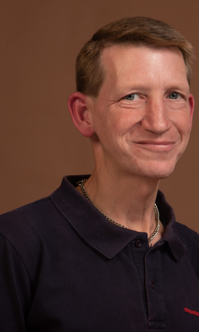 Ein blonder Mann im Polohemd lacht in die Kamera