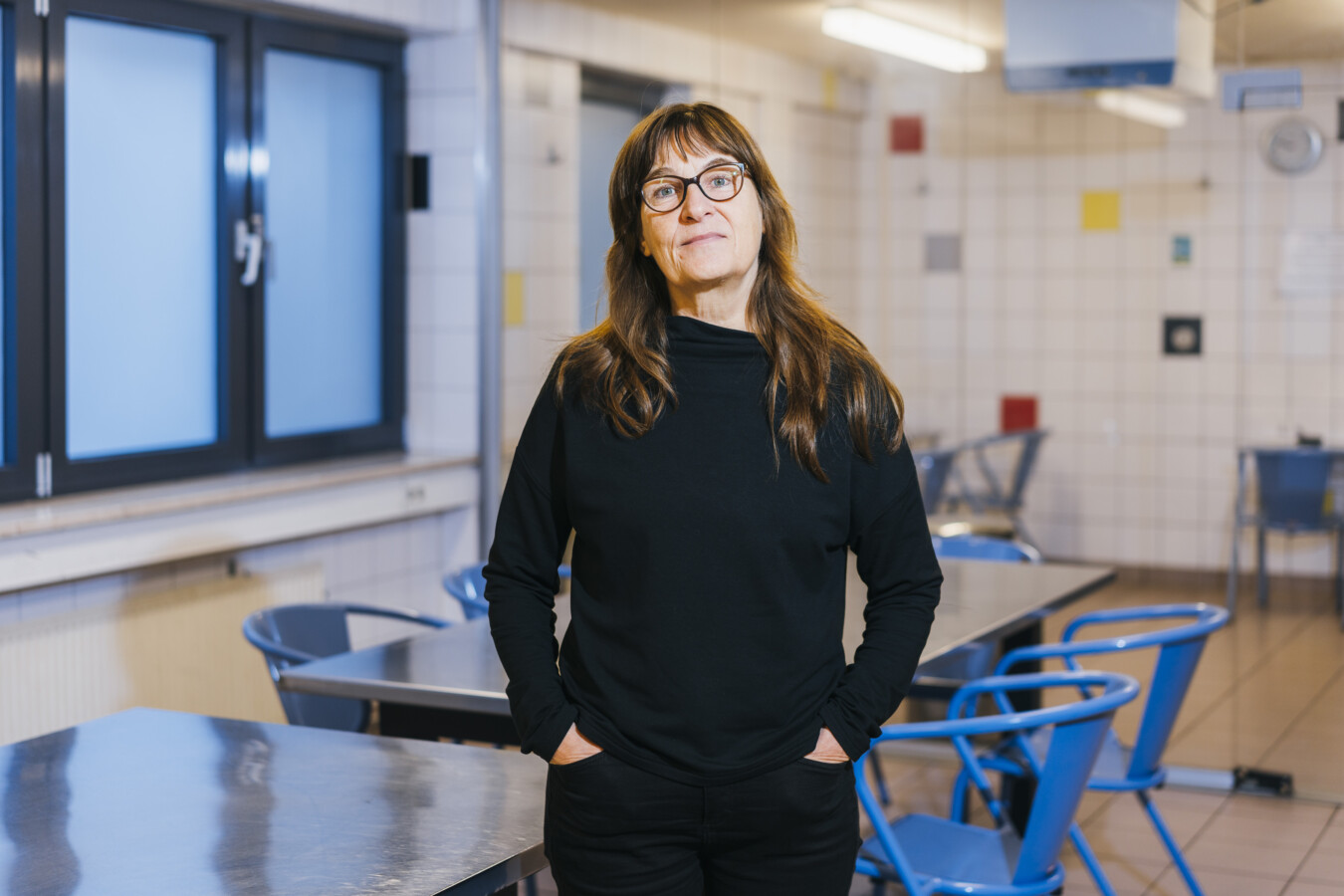 Eine Frau mit Brille steht vor einem Tisch aus Metall in einem gefliesten Raum