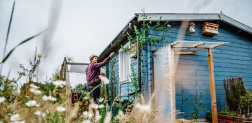 Ein Mann mit Hut steht vor einer blauen Gartenlaube