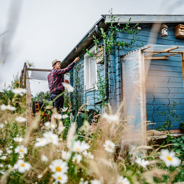 Ein Mann mit Hut steht vor einer blauen Gartenlaube