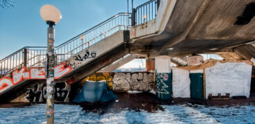 Ein Zelt steht unter einer Brücke, davor liegt Schnee