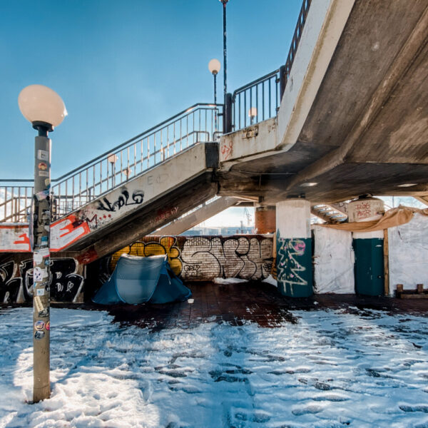 Ein Zelt steht unter einer Brücke, davor liegt Schnee
