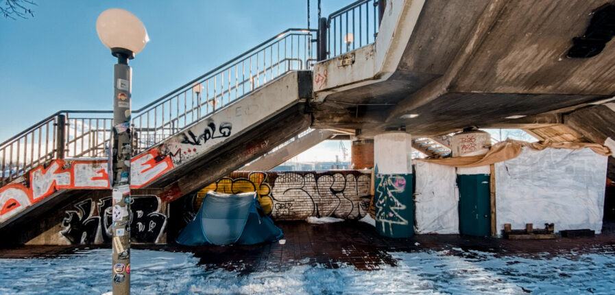 Ein Zelt steht unter einer Brücke, davor liegt Schnee