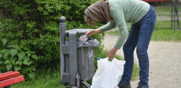 Eine Frau zieht eine Pfandflasche aus einem Mülleimer heraus.