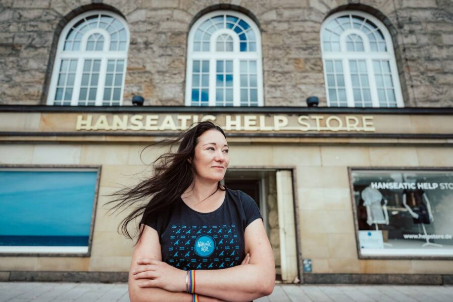 Eine Frau steht vor einem Gebäude mit dem Schild "Hanseatic Help Store"