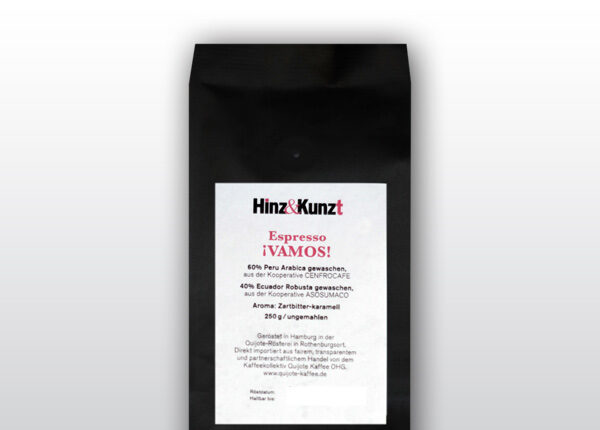 Das Bild zeigt eine schwarze Kaffeeverpackung mit einem weißen Etikett in der Mitte. Auf dem Etikett steht in roter und schwarzer Schrift "Hinz & Kunzt Espresso ¡VAMOS!". Darunter sind Details zum Kaffee aufgeführt