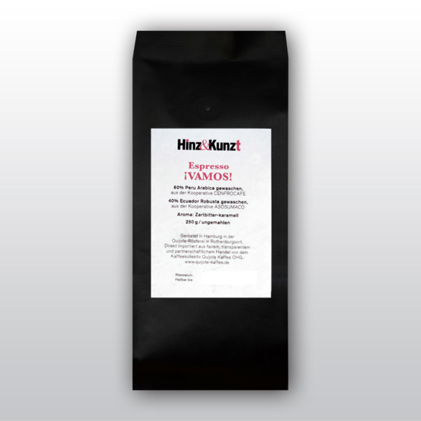Das Bild zeigt eine schwarze Kaffeeverpackung mit einem weißen Etikett in der Mitte. Auf dem Etikett steht in roter und schwarzer Schrift "Hinz & Kunzt Espresso ¡VAMOS!". Darunter sind Details zum Kaffee aufgeführt