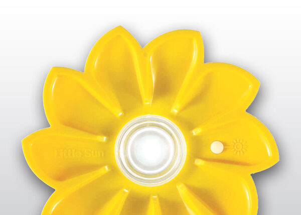 Das gezeigte Bild ist eine gelbe, blumenförmige Solarleuchte mit einer zentralen, transparenten Kapsel, die ein Leuchtmittel enthält, und einem kleinen, runden Schalter mit Sonnensymbol und dem Namen „little sun“ auf einem der Blütenblätter. Ein weiser Druckknopf ist direkt daneben.