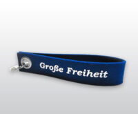 Das abgebildete Objekt ist ein dunkelblauer Schlüsselanhänger mit weißer Aufschrift „Große Freiheit“. Auf der anderen Seite befindet sich die Aufschrift „Hinz&Kunzt“ sowie der Herstellername „dekooop“.