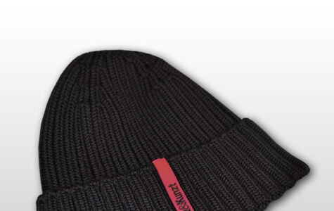 Die Abbildung zeigt eine dunkelblaue Strickmütze mit einem magentafarbenen Etikett, auf dem in schwarzer Schrift "Hinz&Kunzt" steht.