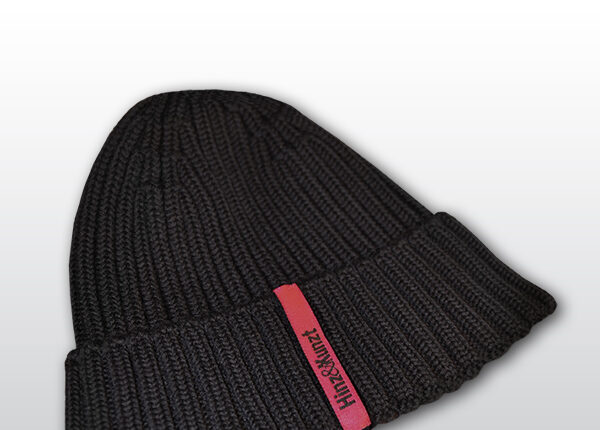 Die Abbildung zeigt eine dunkelblaue Strickmütze mit einem magentafarbenen Etikett, auf dem in schwarzer Schrift "Hinz&Kunzt" steht.