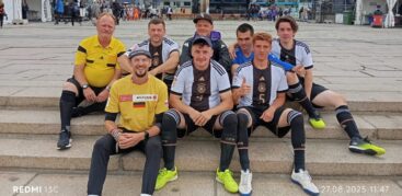 Das Deutsche Straßenfußball-Nationalteam sitzt auf einem Platz auf einer Treppe und grinst in die Kamera.