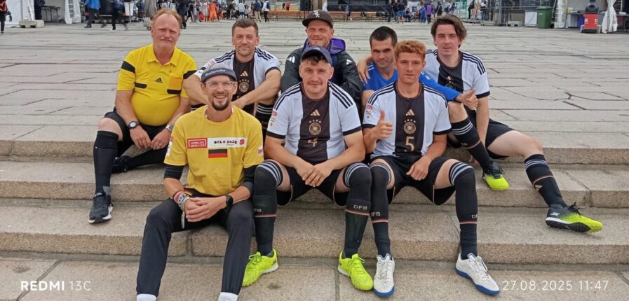 Das Deutsche Straßenfußball-Nationalteam sitzt auf einem Platz auf einer Treppe und grinst in die Kamera.