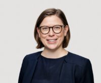 Eine Frau in dunkelblauem Sacko lächelt freundlich in die Kamera