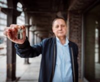 Ein Mann im blauen Hemd zeigt einen Wohnungsschlüssel in die Kamera