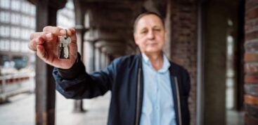 Ein Mann im blauen Hemd zeigt einen Wohnungsschlüssel in die Kamera