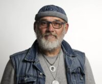 Ein Mann mit grauem Bart, Brille und einer Mütze mit der Aufschrift "Moin"