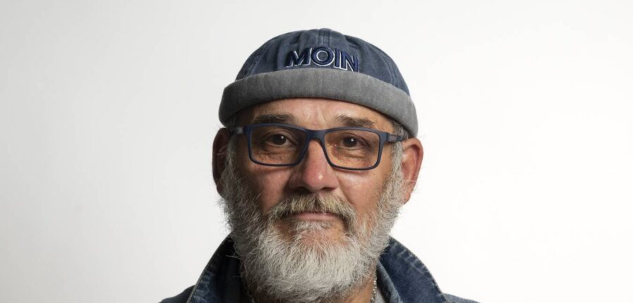 Ein Mann mit grauem Bart, Brille und einer Mütze mit der Aufschrift "Moin"