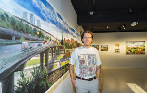 Ein Mann im weißen T-Shirt steht vor einem Gemälde und schaut in die Kamera