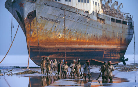 Ein riesiges rostiges Schiff lieft trocken davor waten Männer durch knietiefes Wasser