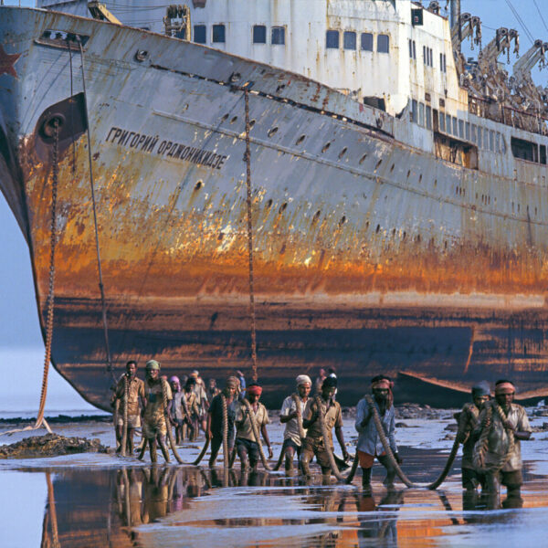 Ein riesiges rostiges Schiff lieft trocken davor waten Männer durch knietiefes Wasser