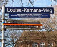Zwei Straßenschilder, "Woermannsweg" ist mit Klebeband überklebt, darüber steht "Louisa-Kamana-Weg"