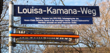 Zwei Straßenschilder, "Woermannsweg" ist mit Klebeband überklebt, darüber steht "Louisa-Kamana-Weg"