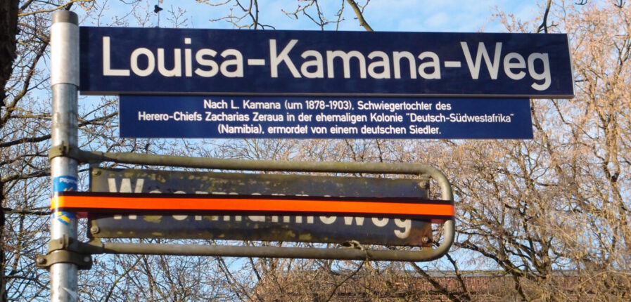 Zwei Straßenschilder, "Woermannsweg" ist mit Klebeband überklebt, darüber steht "Louisa-Kamana-Weg"
