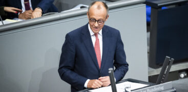 Ein Mann im dunkelblauen Anzug mit rot-weiß gemusterter Krawatte steht am Rednerpult des Bundestags