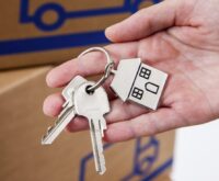 Hand hält Hausschlüsselanhänger in Hausform aus Metall