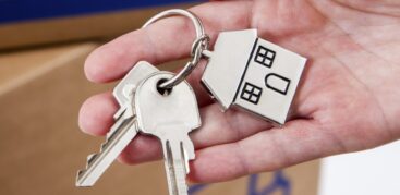 Hand hält Hausschlüsselanhänger in Hausform aus Metall