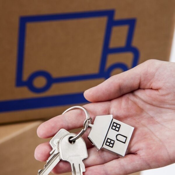 Hand hält Hausschlüsselanhänger in Hausform aus Metall